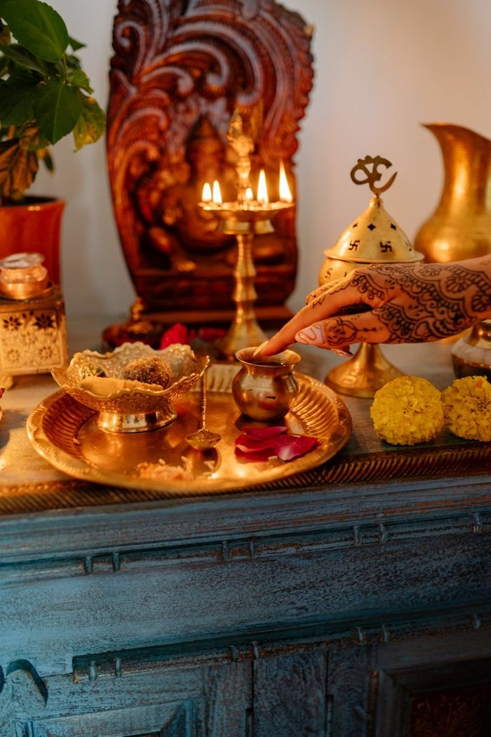 A decorated hand placing offerings on a traditional Hindu altar with candles and brassware.